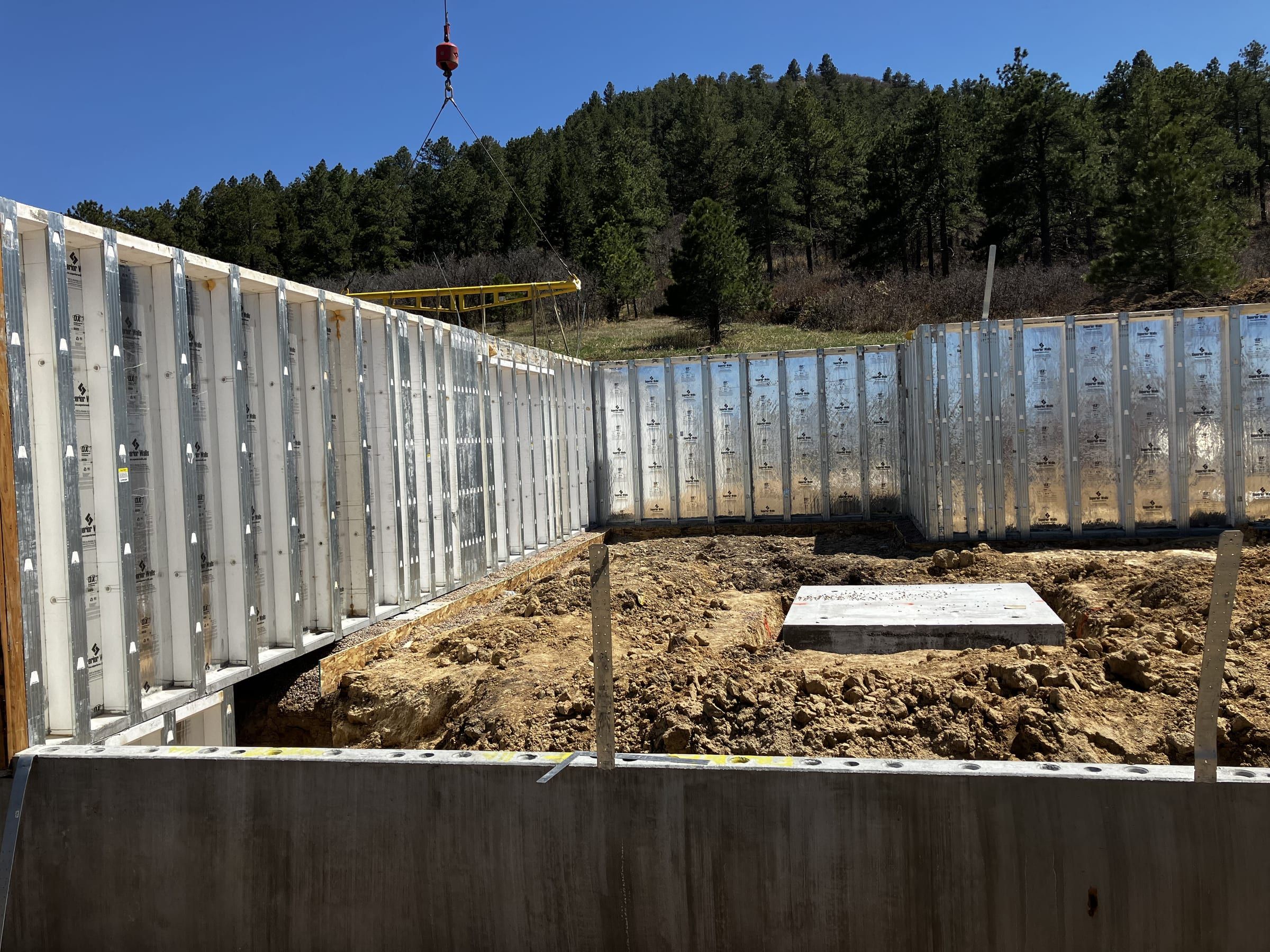 Foundation wall forms set in an excavation, with pine-covered hills behind
