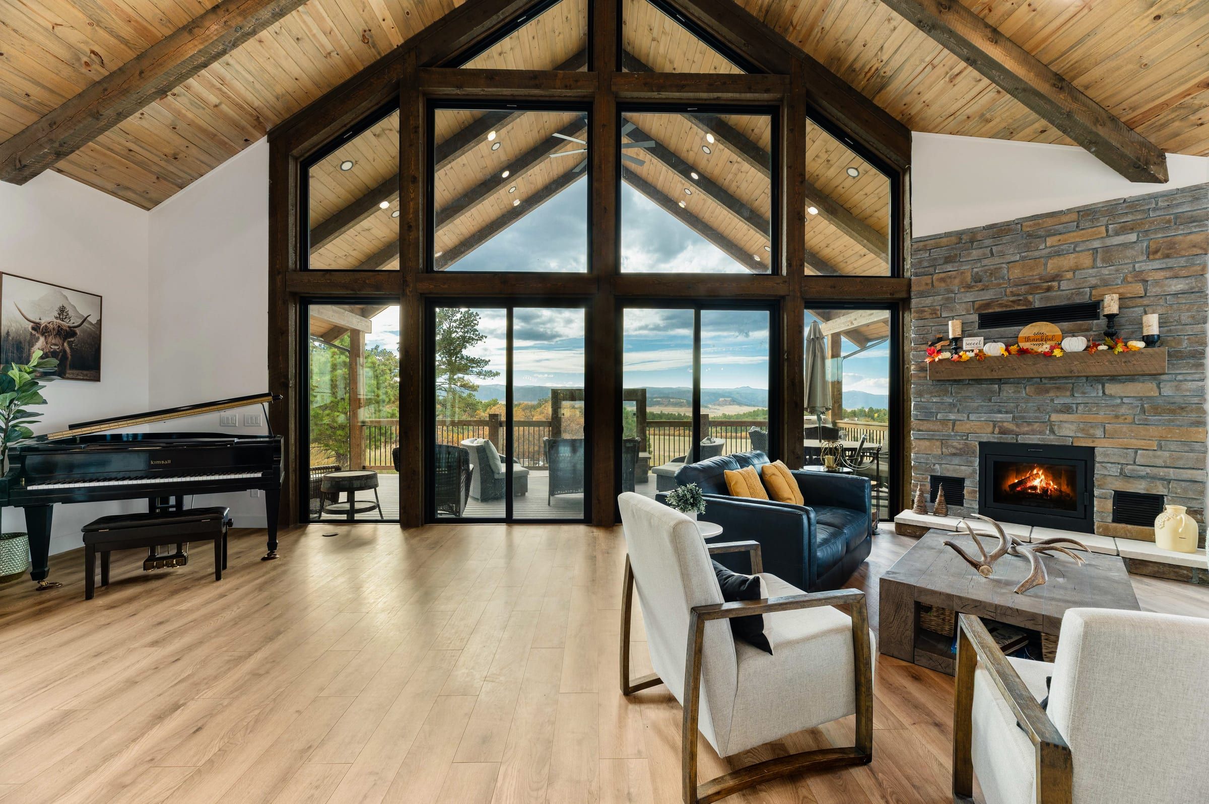 Great room with a timber-framed gable window wall, stone fireplace and wood ceiling