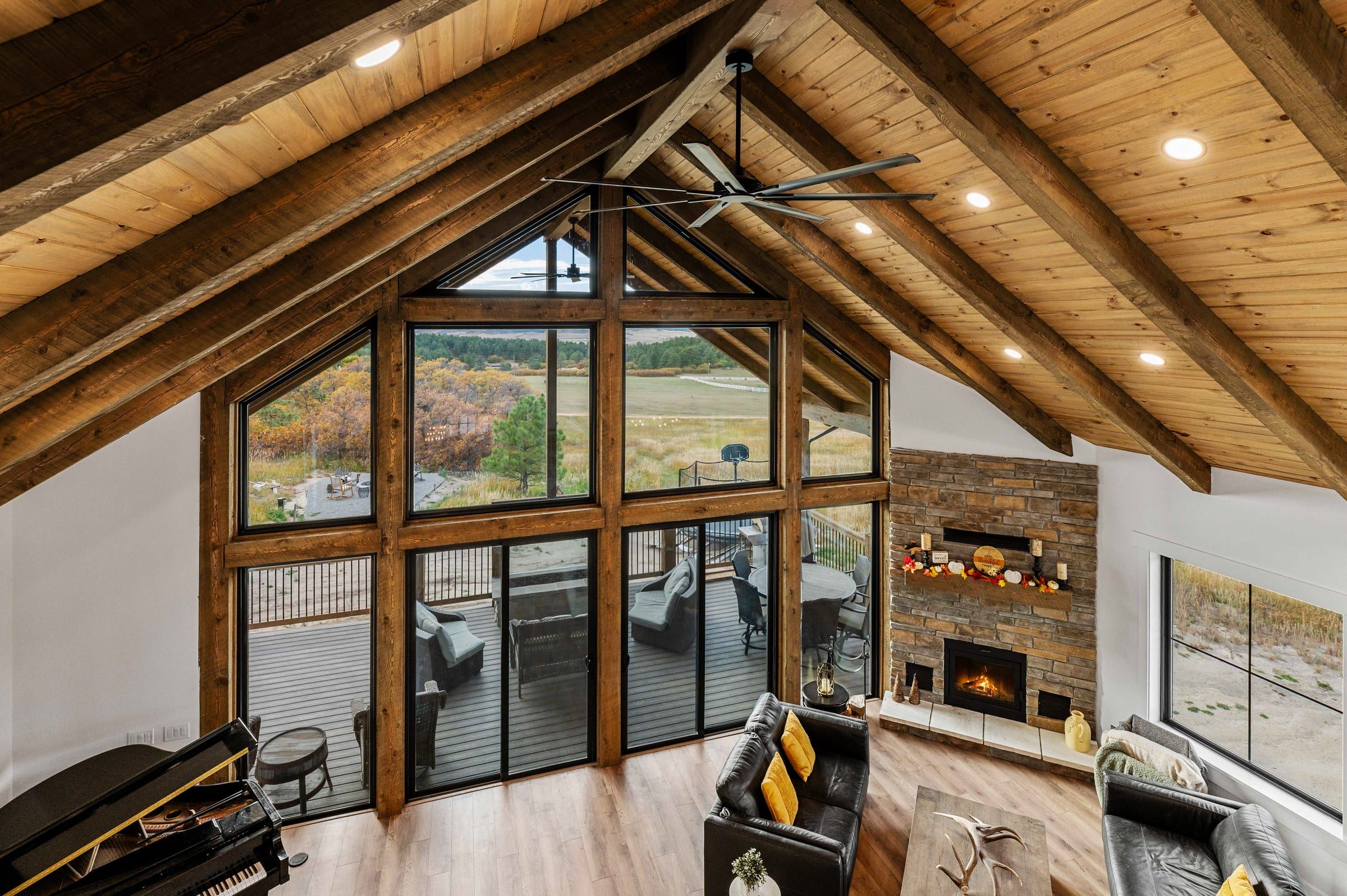 Vaulted great room with exposed timber rafters, a tall gable window wall and a stone fireplace