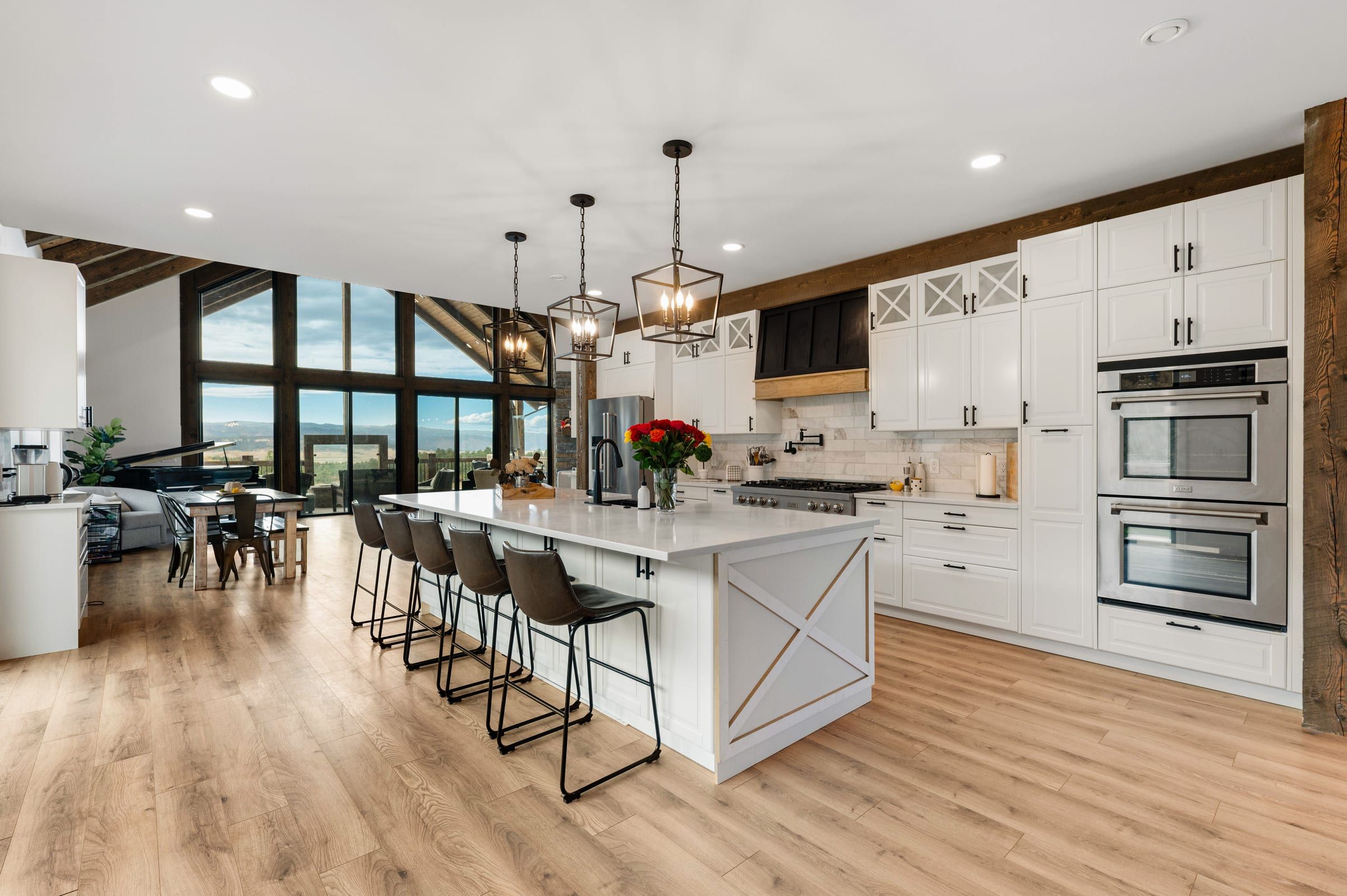 White kitchen with a long island, pendant lights, double wall ovens and a view through the gable windows