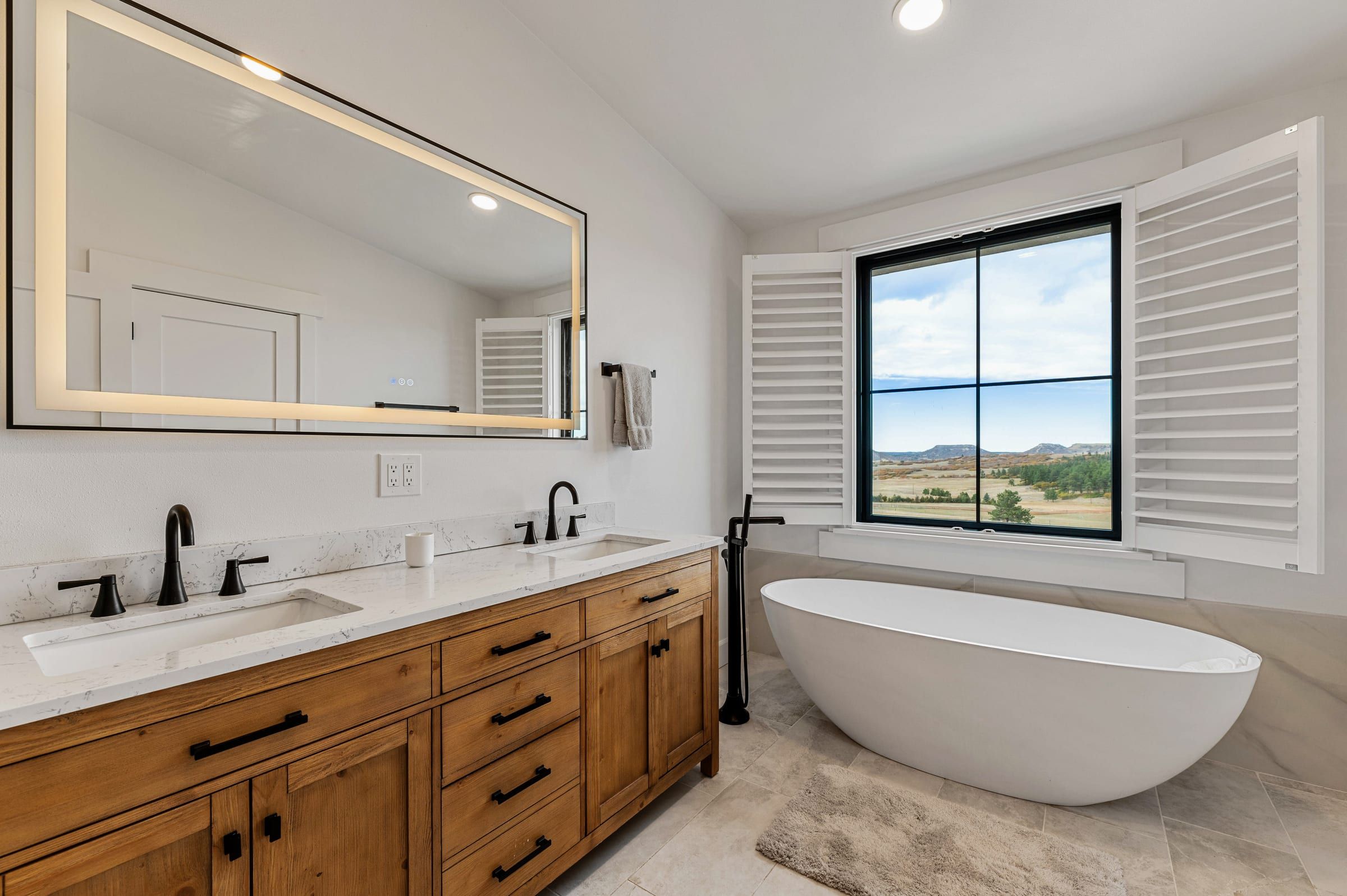 Primary bath with a freestanding tub, double wood vanity and a window to the hills
